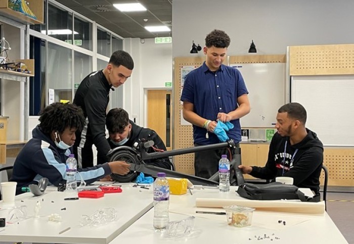 Image of 5 teenagers behind a table looking at the e-scooter they are building